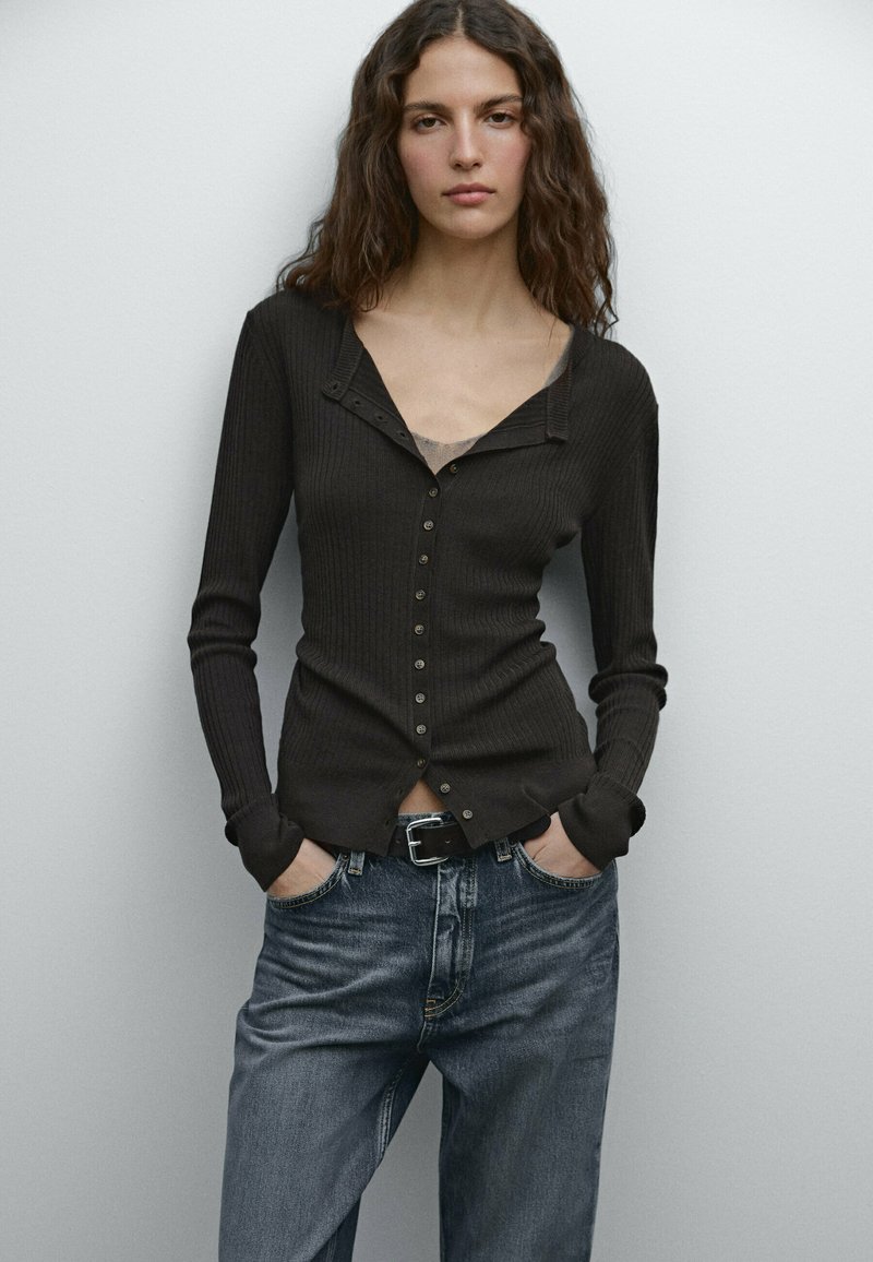 Donker geribbelde lange mouw cardigan met een knoopsluiting, V-hals en slim fit, gecombineerd met lichtblauwe denim jeans.
