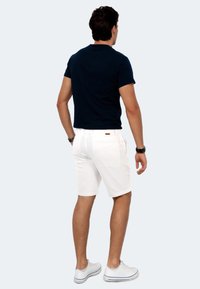 Marineblaue Kurzarm-T-Shirt kombiniert mit weißen Shorts. Das T-Shirt hat eine klassische Passform, die Shorts haben zwei Gesäßtaschen und eine dezente Textur.