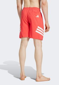 Bañador rojo con cintura elástica y bolsillo trasero, que presenta tres rayas diagonales blancas en el costado para contraste.