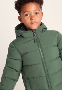 Green puffer jacket with a hood, featuring a zip front, quilted texture, and side pockets. Lightweight with a smooth finish.