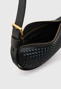 Svart läderhandväska med en texturerad pyramiddesign, guldfärgad dragkedja och rem. Interiören har flera fack och en slät foder.