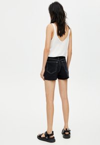 Zwarte denim shorts met rafelige rand, achterzakken en witte stiksels, gecombineerd met een witte tanktop en zwarte sandalen.