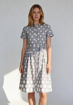Vrouw draagt een knielange, korte mouwen, grijze jurk met grote witte polka dots en een bijpassende stoffen riem gestrikt in de taille.