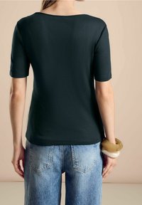 Mörkgrön kortärmad topp med bred halsringning, i kombination med högmidjade ljusblå denimjeans. Slät textur och avslappnad passform.