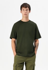 Dark green cotton t-shirt with a crew neckline and short sleeves, featuring a relaxed fit. Worn with green cargo pants.