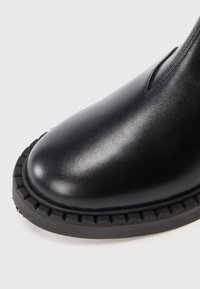 Botte en cuir noir avec un bout rond, des détails cousus et une semelle en caoutchouc épaisse avec un bord texturé pour une meilleure adhérence et durabilité.