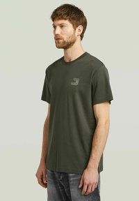 Olijfgroene katoenen t-shirt met een ronde hals, korte mouwen en een klein gedrukt logo op de borst. Zachte textuur, casual pasvorm.