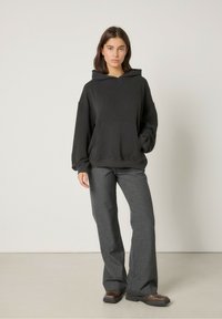 Felpa nera con cappuccio e tasca frontale, vestibilità rilassata e texture a coste, abbinata a pantaloni grigi a zampa d'elefante e scarpe marroni, design minimalista.