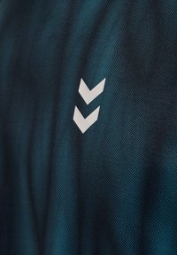 Donker teal gekleurd, gestructureerd stof met twee witte naar beneden gerichte chevrons, verticaal gecentreerd op het oppervlak.