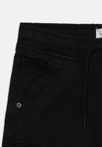 Pantalons de jogging noirs avec taille élastique, cordon de serrage et poches latérales avec des accents métalliques. Texture lisse et design décontracté.
