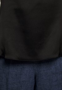 Ourlet supérieur noir sur un jean en denim bleu foncé, montrant les détails de texture et de couture des deux tissus.