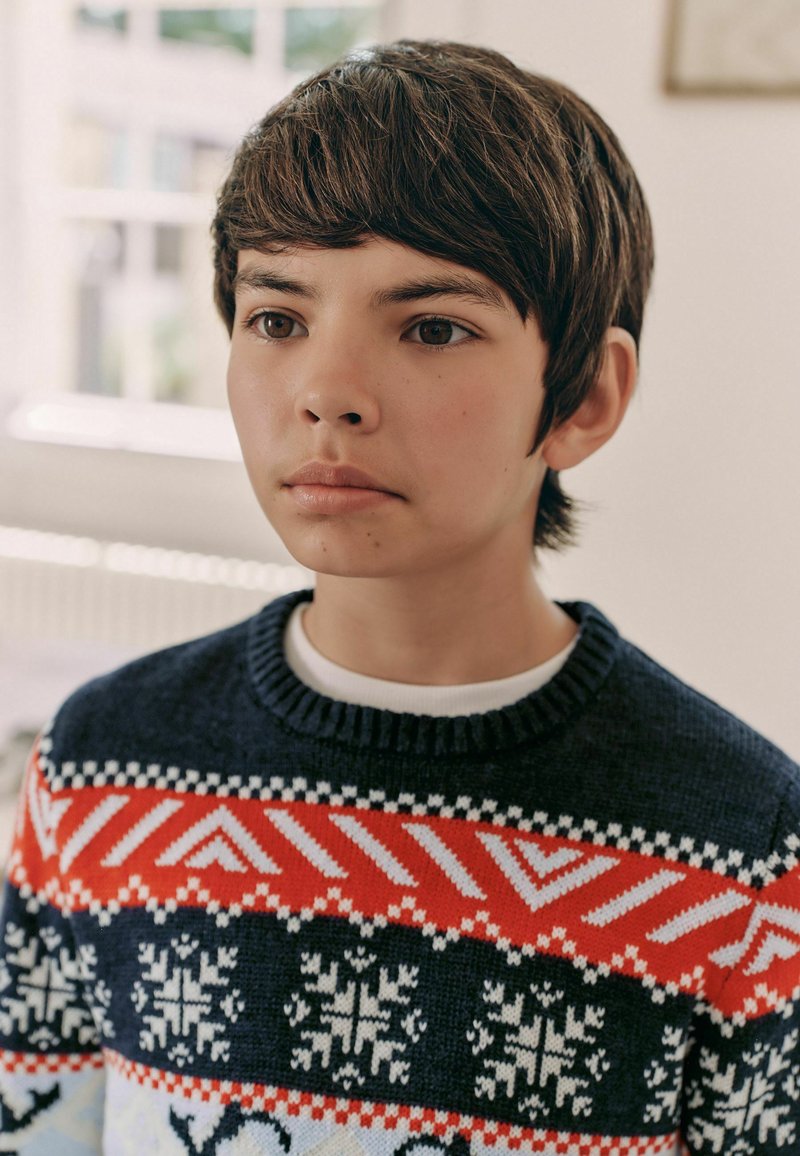 Sweter dzianinowy w kolorze granatowym z czerwonymi, białymi i jasnoniebieskimi geometrycznymi wzorami oraz motywami płatków śniegu; klasyczny dekolt typu crew neck.