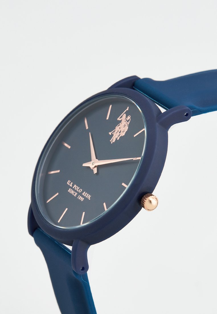 Montre avec bracelet en silicone bleu marine et accents dorés, cadran rond, design minimaliste, visage bleu foncé, aiguilles dorées et détail du logo.