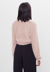 Fuzzy ljusbeige tröja med långa ärmar, rund halsringning och ribbat avslut; kombinerad med svarta byxor med elastisk midja.