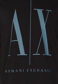 Svart tyg med stora ljusblå "A | X" bokstäver och texten "Armani Exchange" tryckt nedanför.