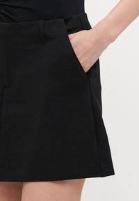 Zwarte shorts van een gladde stof, met zijzakken, een recht model en een tailleband met riemlussen. Geen zichtbare patronen of accenten.