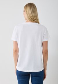 T-shirt bianca in cotone con maniche corte e collo rotondo, caratterizzata da una texture liscia e una vestibilità rilassata, mostrata da dietro.