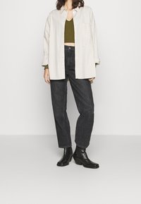 Ylitysmitalla raidallinen paita vaaleassa kerma- ja beigevärissä, oliivinvihreä crop-top, mustat korkeavyötäröiset farkut ja mustat nilkkurit, joissa on kevyt korko.