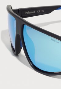 Occhiali da sole sportivi con montatura nera e lenti a specchio blu. Gli accenti notevoli includono le stanghette curve e il logo sul telaio.