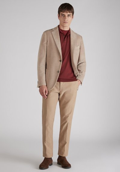 Beżowa marynarka z korduroy połączona z bordową koszulką polo i jasnymi beżowymi spodniami. Brązowe zamszowe botki za kostkę dopełniają strój.