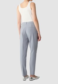 Lichtgrijze op maat gemaakte broek met een gladde textuur, voorzien van twee achterzakken, gecombineerd met een witte tanktop en zilveren ballerina's.