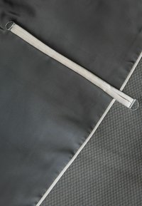 Tela negra con una textura suave que presenta un detalle de cremallera blanca estrecha. El diseño incluye un sutil brillo sobre un fondo gris con patrón.