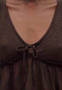 Κοντινό πλάνο ενός ατόμου που φοράει καφέ τοπ με V-λαιμόκοψη, με δεμένο φιόγκο στο λαιμό και ραμμένο ύφασμα κάτω από το στήθος.