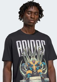 Mustmustri musta t-särk, millel on graafiline trükk tegelasest, kes istub troonil, ja peal on julged "ADIDAS" tekst valgete tähtedega.