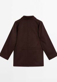 Giacca lunga a maniche e marrone scuro con taglio dritto, dettagli delle cuciture sul retro e un piccolo colletto rialzato, posata su uno sfondo bianco.