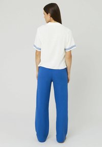 Haut blanc à manches courtes avec des accents brodés bleus aux poignets, associé à un pantalon large bleu uni, mettant en valeur une coupe décontractée.