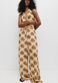 Twee-delig outfit met bloemenprint, bestaande uit een haltertop en wijde broek in beige met bruine patronen; gemaakt van lichtgewicht stof.