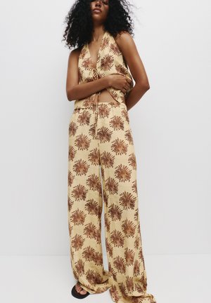 Twee-delig outfit met bloemenprint, bestaande uit een haltertop en wijde broek in beige met bruine patronen; gemaakt van lichtgewicht stof.