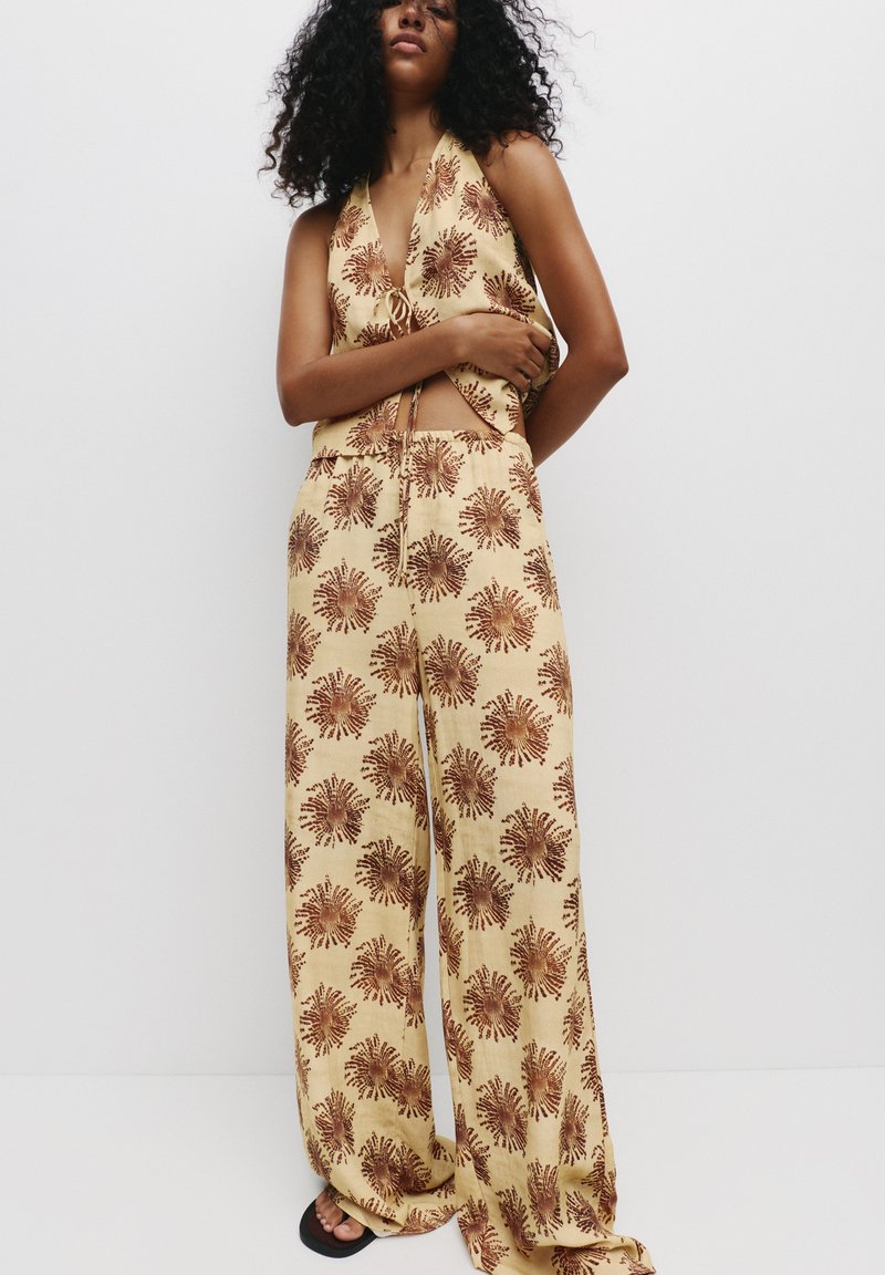 Twee-delig outfit met bloemenprint, bestaande uit een haltertop en wijde broek in beige met bruine patronen; gemaakt van lichtgewicht stof.