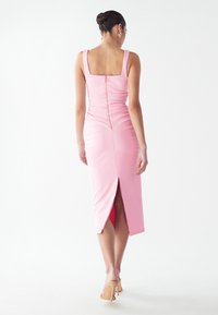 Robe rose ajustée sans manches avec un décolleté carré, en tissu texturé, et une fermeture éclair au dos ; présente une fente haute sur la jupe.