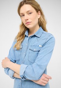 Hele sinine denim-särk, millel on nööpidest sulgemine, kaks rinnataskut ja üles keeratud varrukad. Omab klassikalist kraed ja sileda tekstuuri.