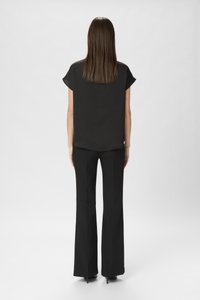 Sort kortærmet bluse med løs pasform, parret med sorte højhalsede bukser. Glat tekstur med et minimalistisk design.