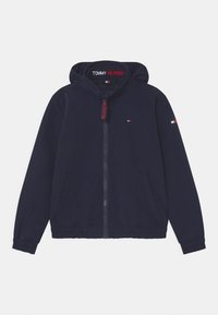 Marineblå hættetrøje med lynlås og elastiske manchetter. Har sidelommer og et logo på brystet. Glat stof med et let design.