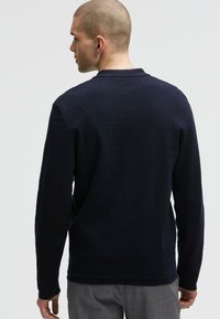 Marineblaues Langarm-Polohemd mit strukturiertem Finish, ausgestattet mit einem flachen Kragen und seitlichen Schlitzen am Saum für optimale Bewegungsfreiheit.