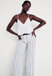 Haut en crochet blanc sans manches avec un ourlet évasé, associé à un pantalon en lin léger à rayures avec une taille à cordon.
