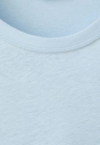 Tissu en coton bleu clair à col rond en gros plan montrant une texture lisse et des coutures fines le long de l'encolure.