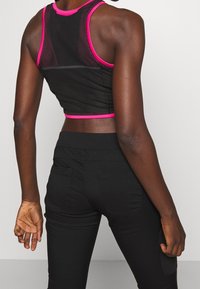 Svart mesh crop top med fuchsia detaljer, racerback-design, i kombination med åtsittande svarta byxor. Tyget verkar luftigt med en strukturerad yta.