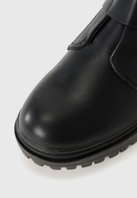 Black leather boot with a smooth texture, rounded toe, and a rugged black outsole featuring deep grooves for traction.