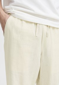 Lyse beige linnedbukser med elastik i taljen, bindebånd og sidelommer, med en blød, struktureret overflade.