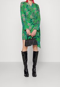 Zielona sukienka w wzory o kroju kopertowym, z długimi rękawami. Połączona z czarną torebką na łańcuszku i błyszczącymi, czarnymi kozakami do kolan.