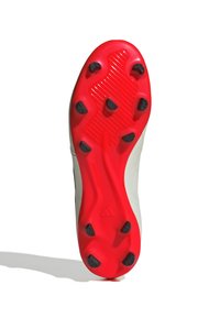 Suela de un botín de fútbol con una parte superior blanca, suela roja con tacos negros, superficie texturizada con ranuras para tracción.