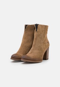 Bottines en suede marron, avec un bout arrondi, une fermeture éclair à l'arrière et un talon empilé. Présente un bord en cuir lisse au niveau du bout.