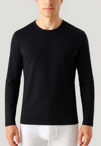 Maglietta nera a maniche lunghe realizzata in tessuto morbido, con scollatura rotonda e un design aderente, abbinata a pantaloni bianchi aderenti.