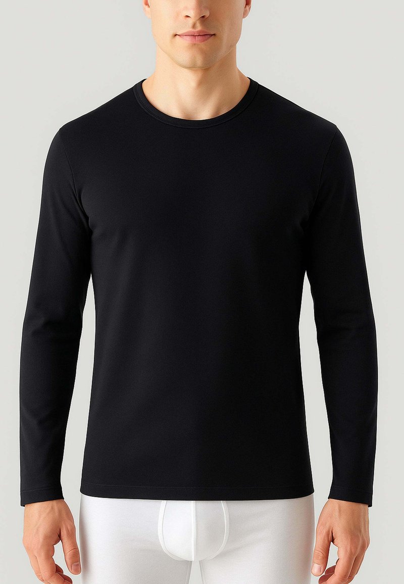 Maglietta nera a maniche lunghe realizzata in tessuto morbido, con scollatura rotonda e un design aderente, abbinata a pantaloni bianchi aderenti.