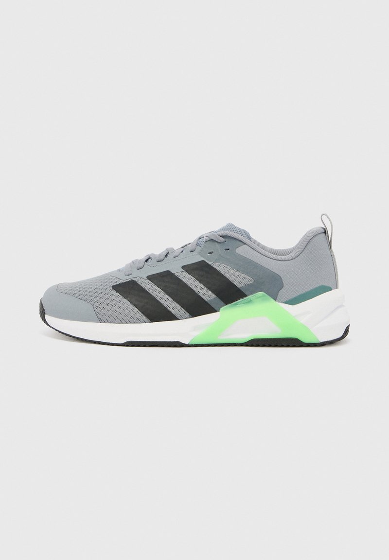 Basket athlétique grise avec des rayures noires, un accent vert sur la semelle blanche et une tige en mesh, vue de profil sur un fond uni.