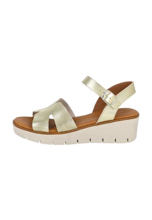 Sandalias de mujer con una parte superior de oro perforada, una correa en el tobillo, plantilla de cuero marrón y una suela cuña de color beige claro con ranuras.